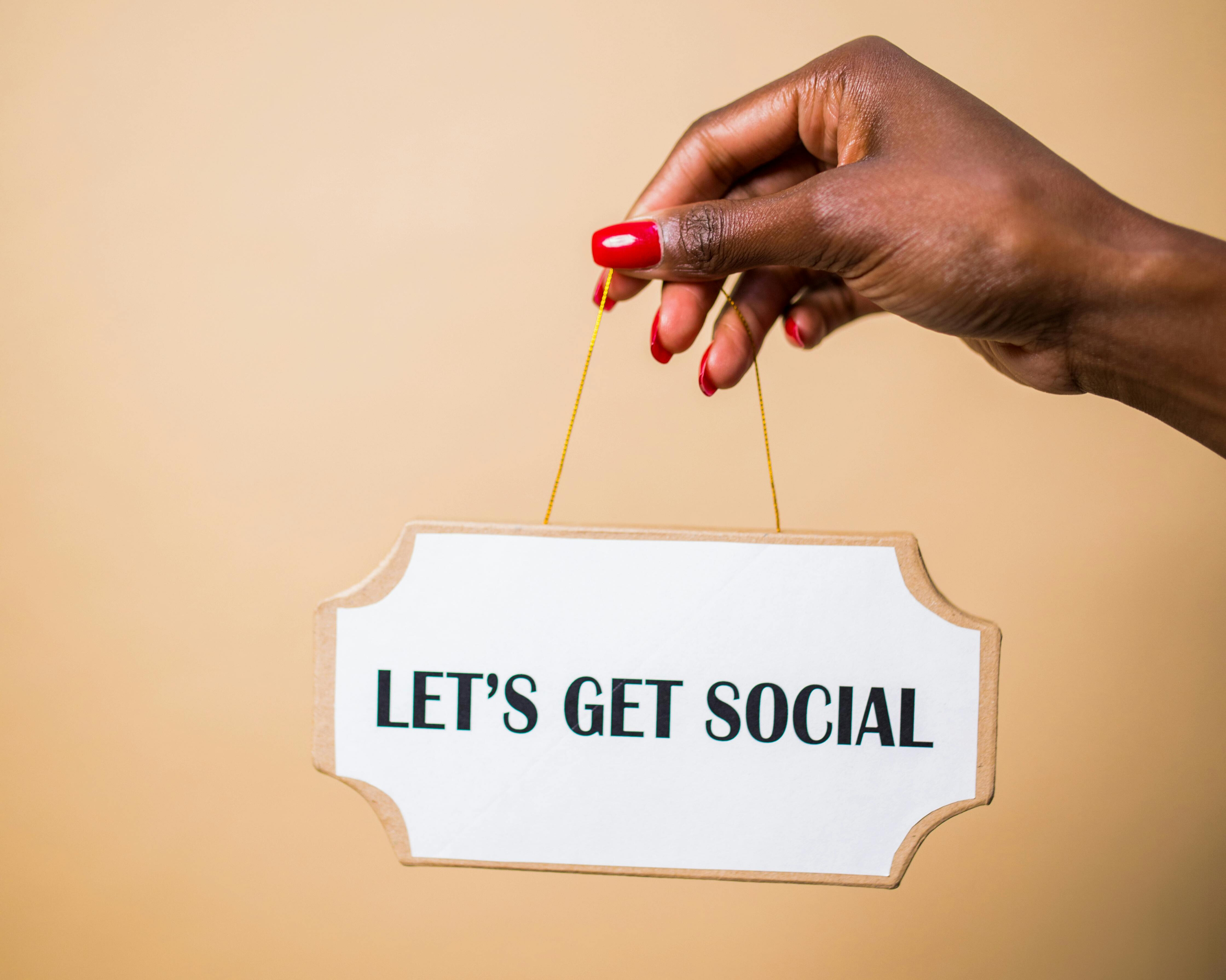 A hand holding a sign that says “LET’S GET SOCIAL” on a beige background, symbolizing the importance of communication and creativity in digital marketing.